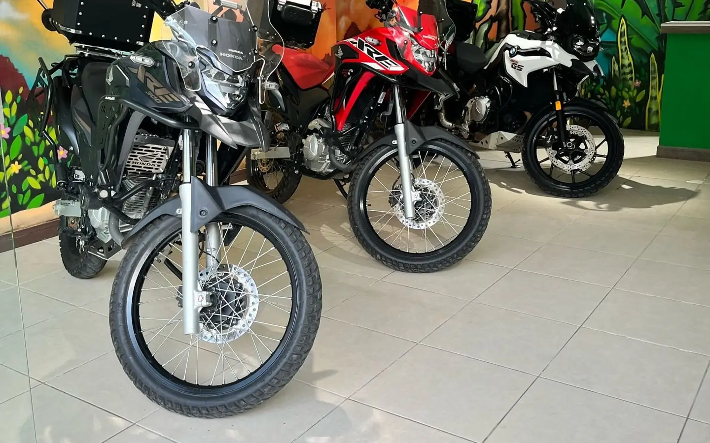 Motos de la flota en la sede, frente al mural de loros y café